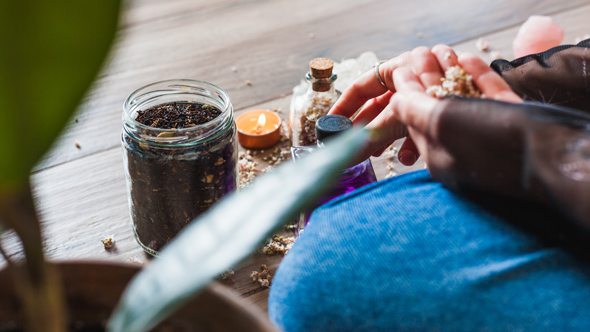Modern young witch practicing spells with herbs and bottles