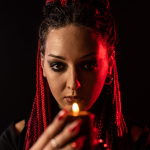 Solitary witch with braids and candle against red light